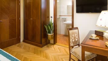 A hotel room with a wooden wardrobe, a potted plant, a dining table with chairs, and a television mounted on the wall.