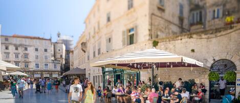 A bustling outdoor cafe area with outdoor seating and umbrellas, surrounded by historic buildings.