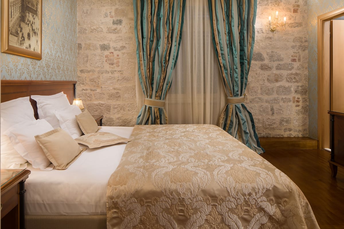 A neatly made bed with a patterned bedspread, a wooden headboard, and a stone wall with a framed picture.