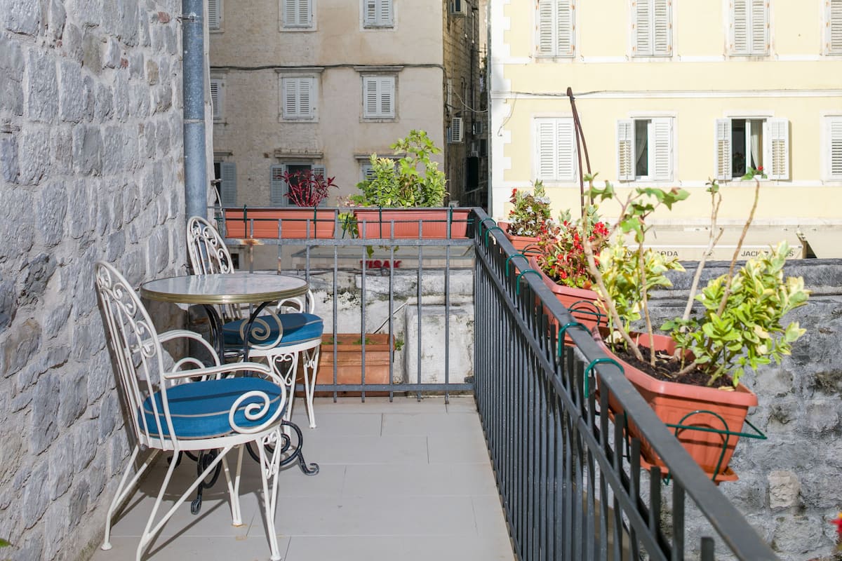 A balcony with a table and chairs, potted plants, and a stone wall.