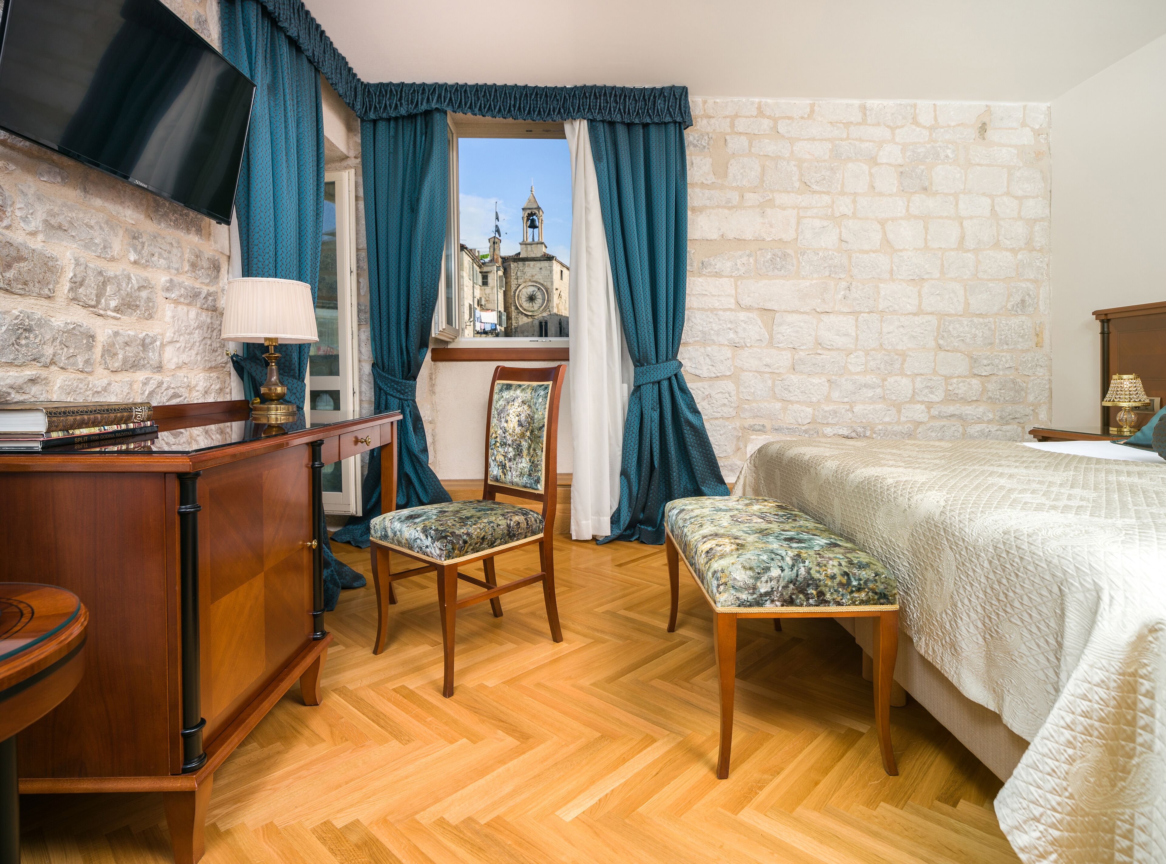 A hotel room with a wooden desk, a chair, a bed, and a stone wall.