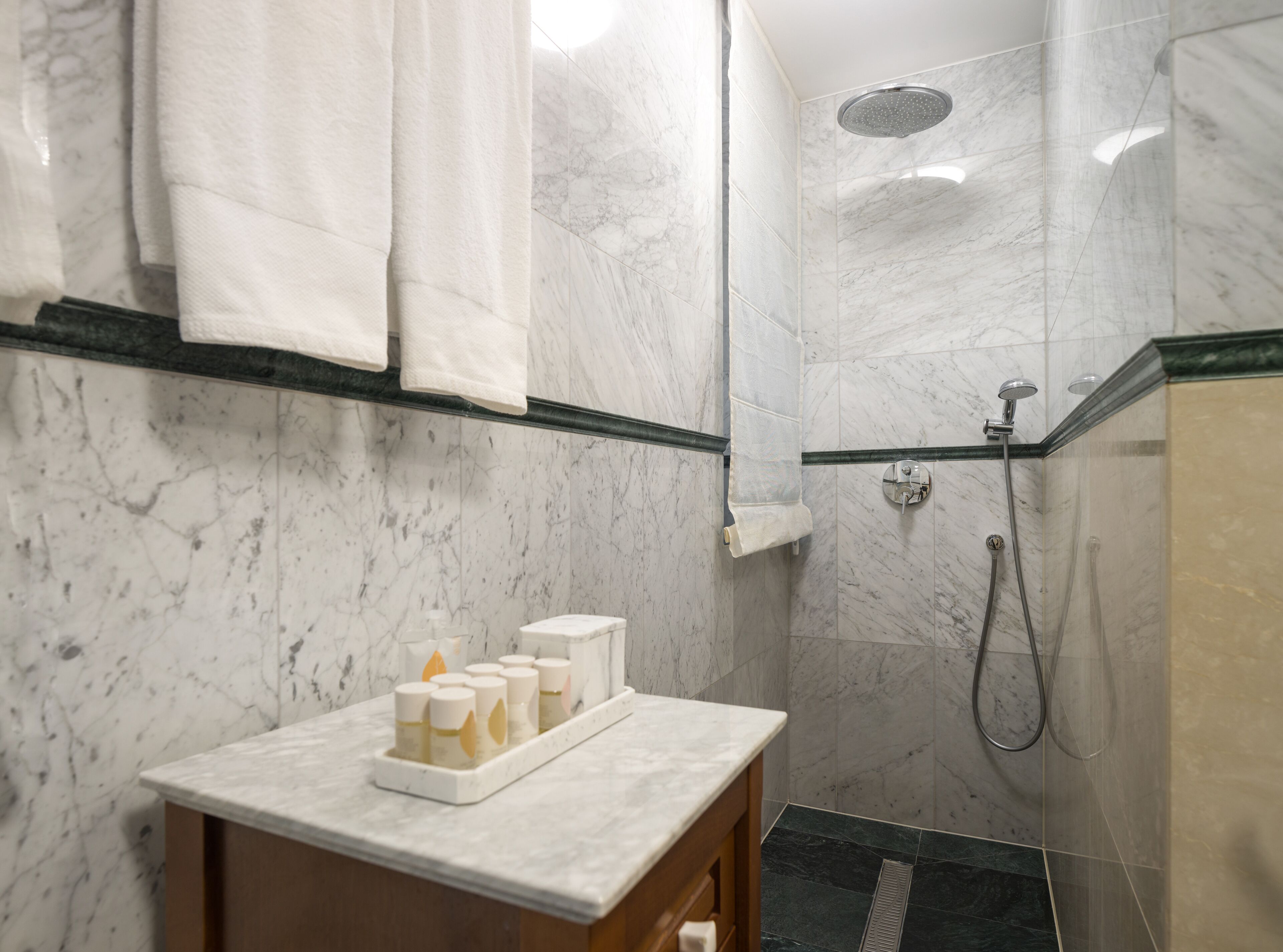 A bathroom with a marble shower, a sink with toiletries, and towels hanging on a rack.