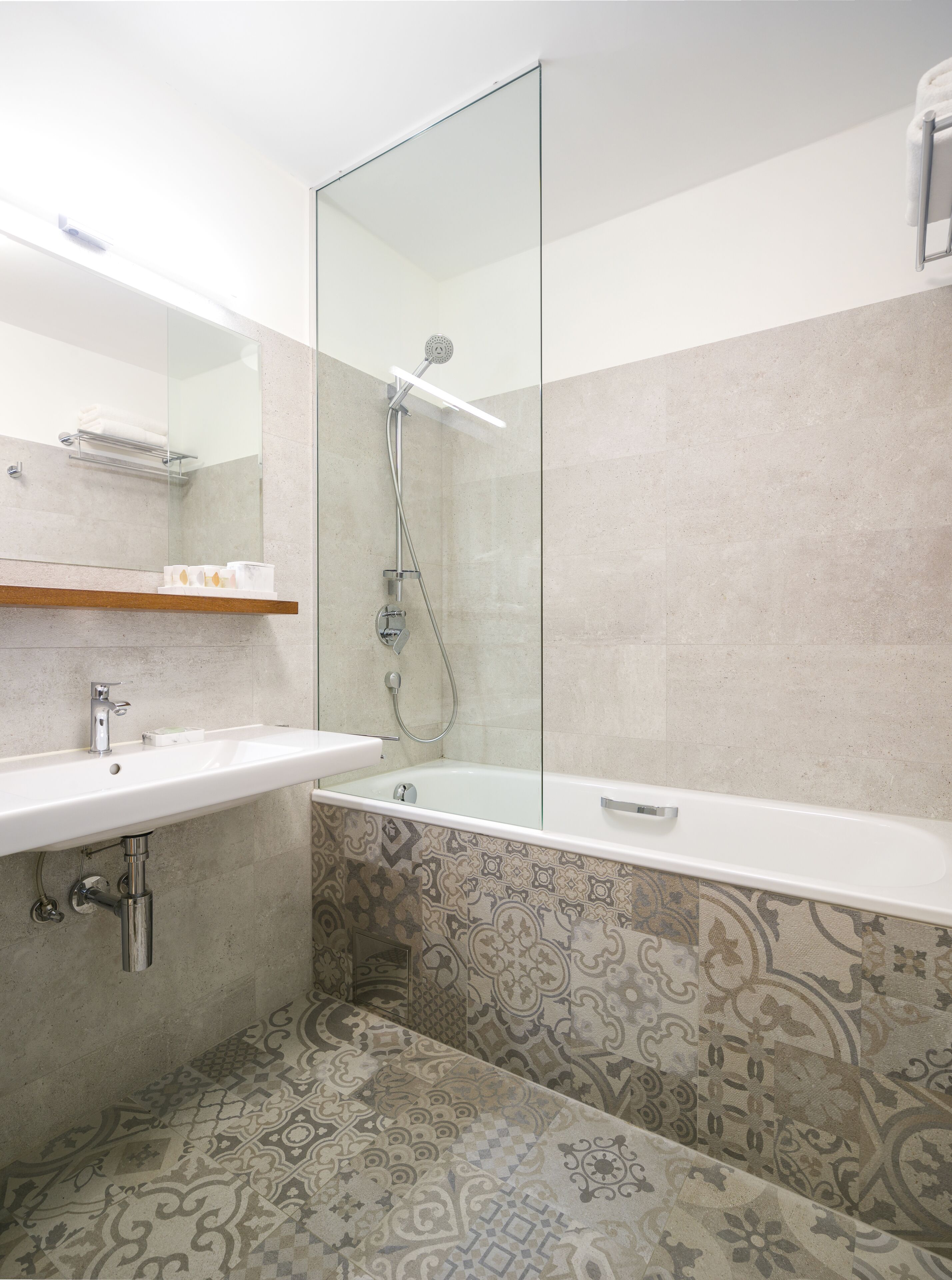 Une salle de bain moderne avec une douche à parois de verre, un lavabo blanc et des carreaux à motifs.