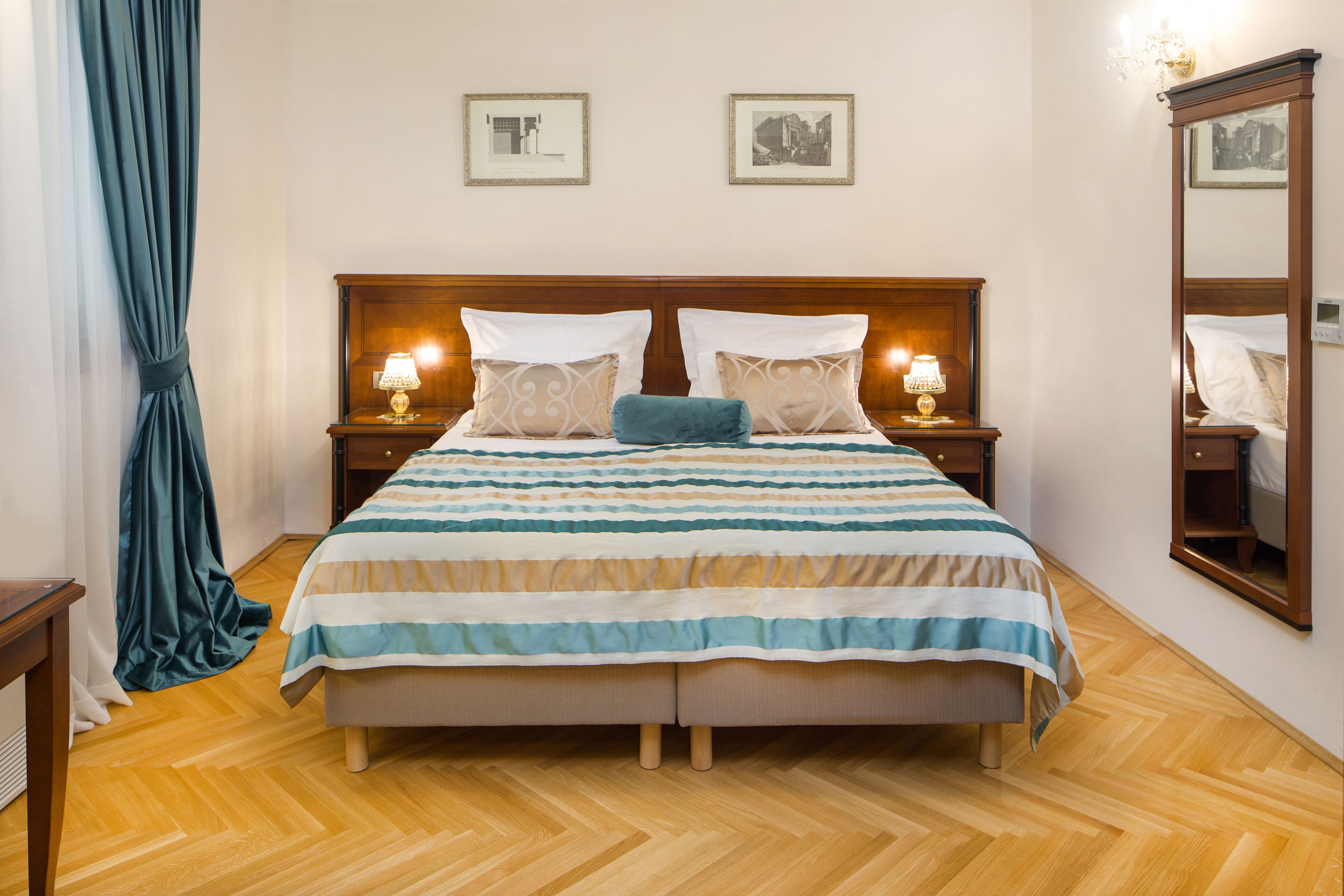 Una cama bien hecha con una colcha a rayas, dos mesitas de noche con lámparas, un espejo grande y dos cuadros enmarcados en la pared.
