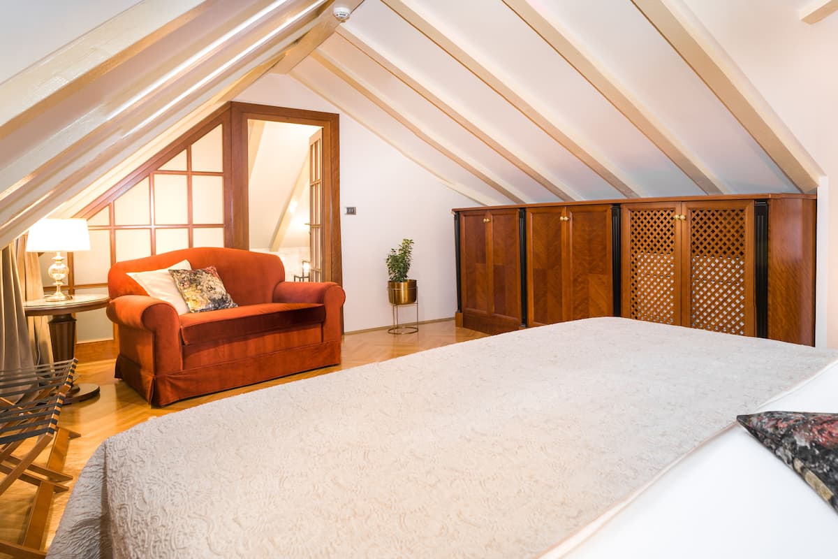A spacious attic bedroom with a large bed, a red sofa, and a wooden wardrobe.