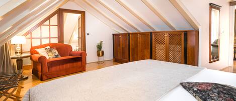 Ein geräumiges Schlafzimmer im Dachgeschoss mit einem großen Bett, einem roten Sofa und einem Holzschrank.