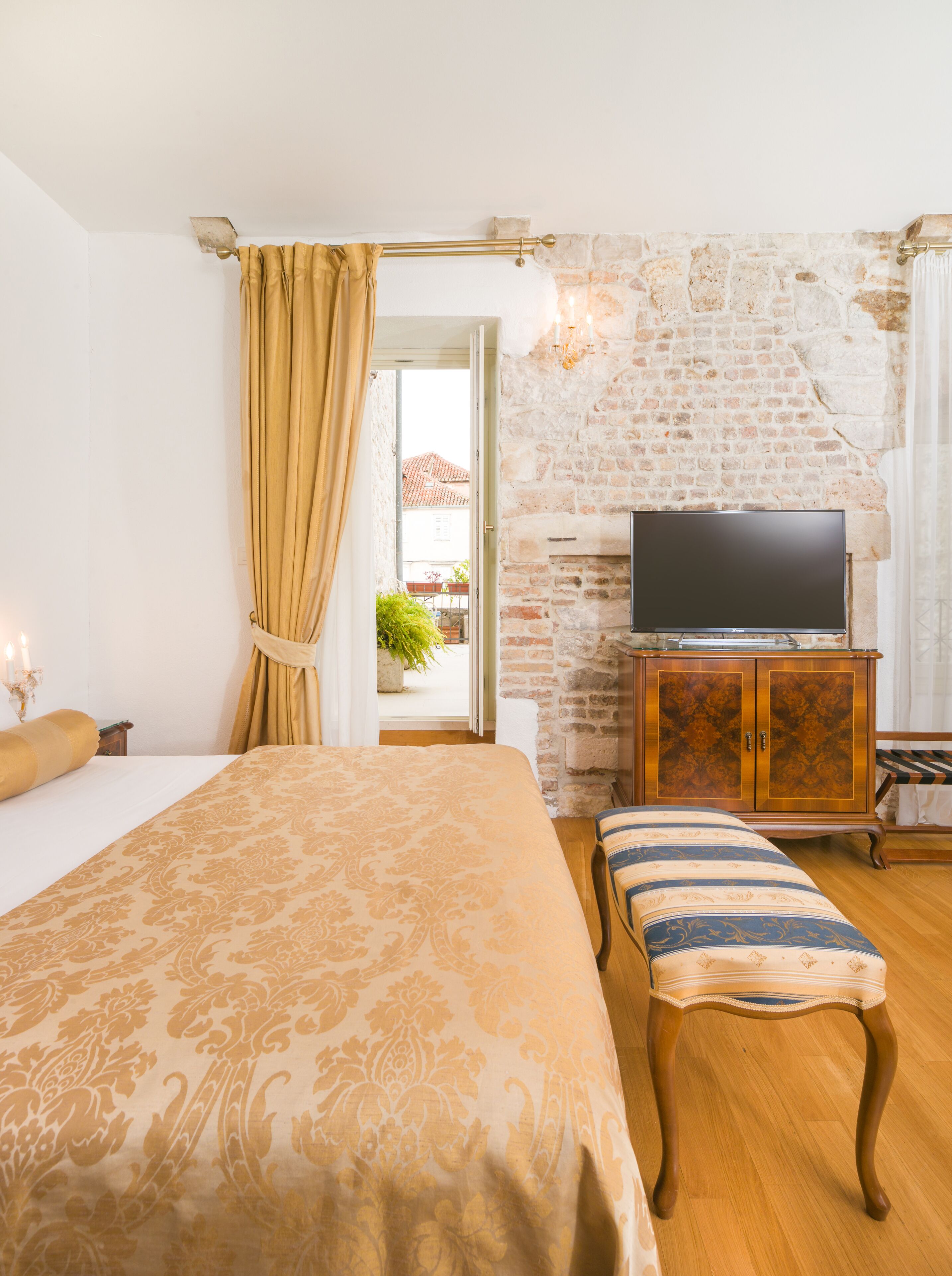 Un dormitorio con una cama grande, un banco de madera, un televisor sobre un mueble y una pared de piedra.