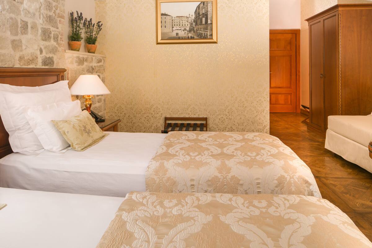 A hotel room with two beds, a stone wall, a framed picture, and a wooden wardrobe.