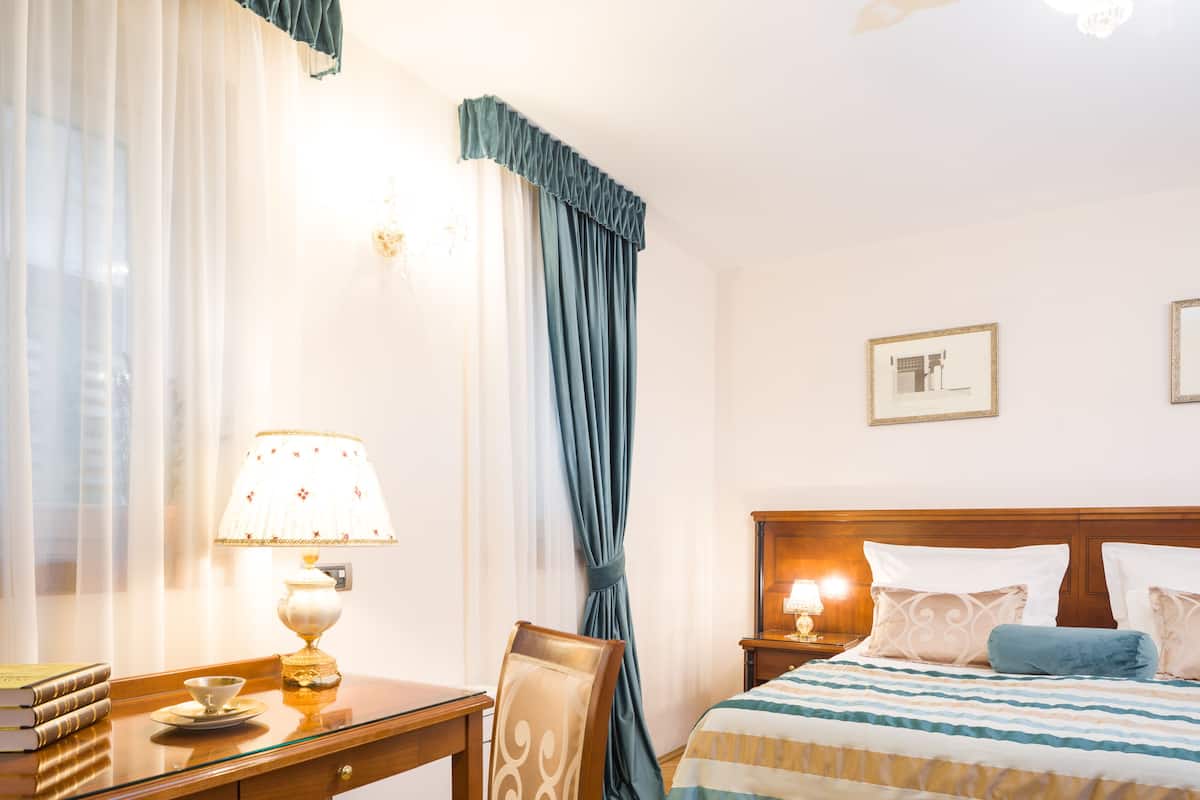 A hotel room with a wooden desk, a chair, a bed with a striped bedspread, and a nightstand with a lamp.