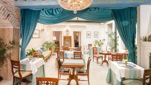 Een eetgedeelte met getoonde tafels, een kroonluchter en blauwe gordijnen.