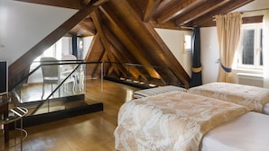 Een slaapkamer met twee bedden, houten balken, een glazen balustrade en uitzicht op het omliggende landschap.