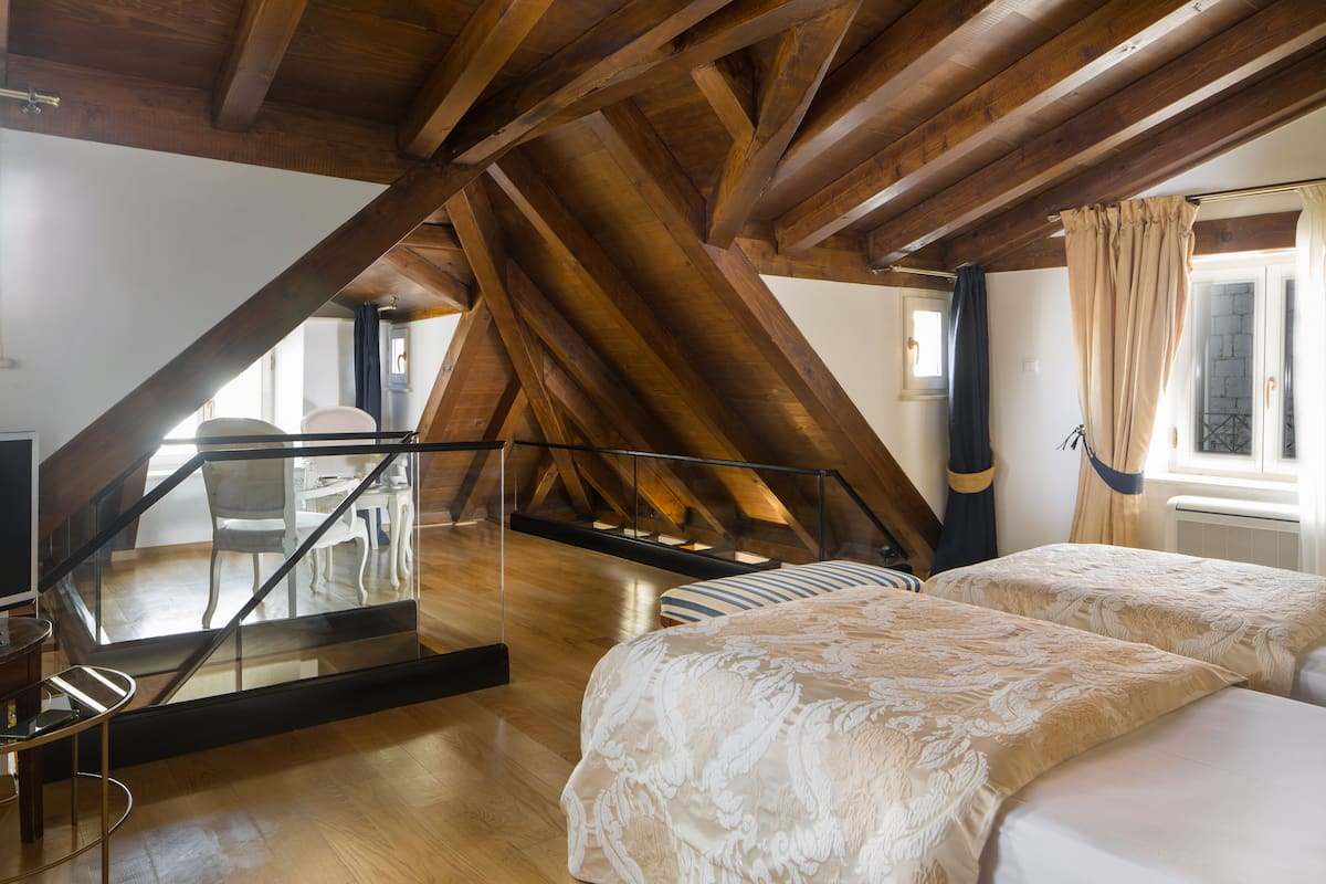A bedroom with two beds, wooden beams, a glass railing, and a view of the outside.