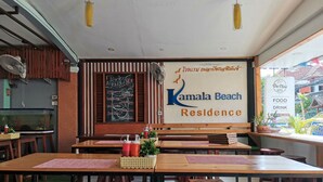 A restaurant with wooden tables and benches, a chalkboard menu, and a sign for Kamala Beach Residence. - Kamala Beach Residence (Kamala)