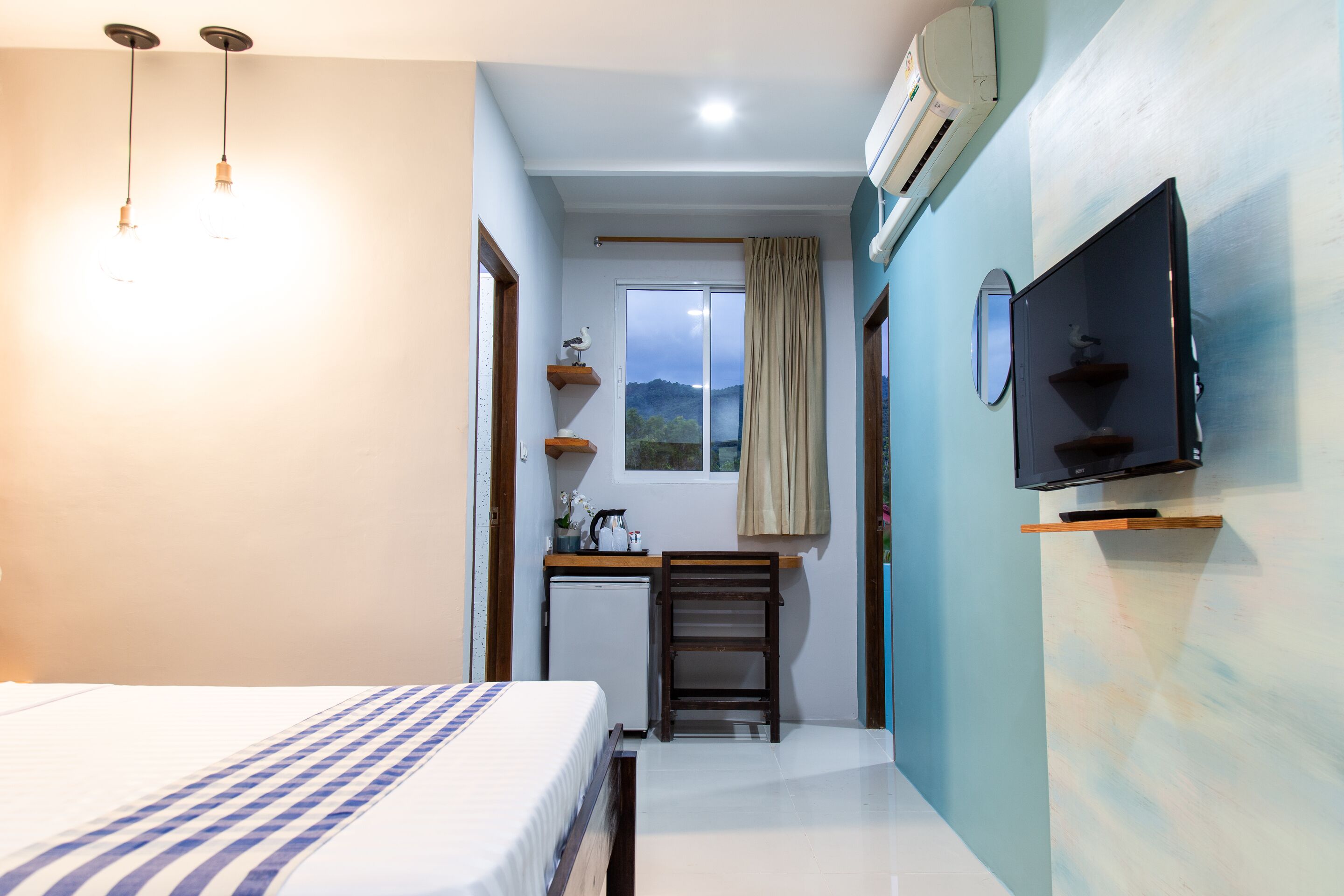 A hotel room with a bed, a desk, a chair, a television, and a window with a view of the mountains.