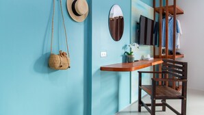 A room with a teal wall, a wooden desk, a chair, a hat, a mirror, and a hanging plant. - Kamala Beach Residence (Kamala)