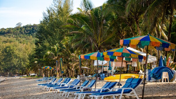 A beach with rows of blue lounge chairs and colorful umbrellas. - Kamala Beach Residence (Kamala)