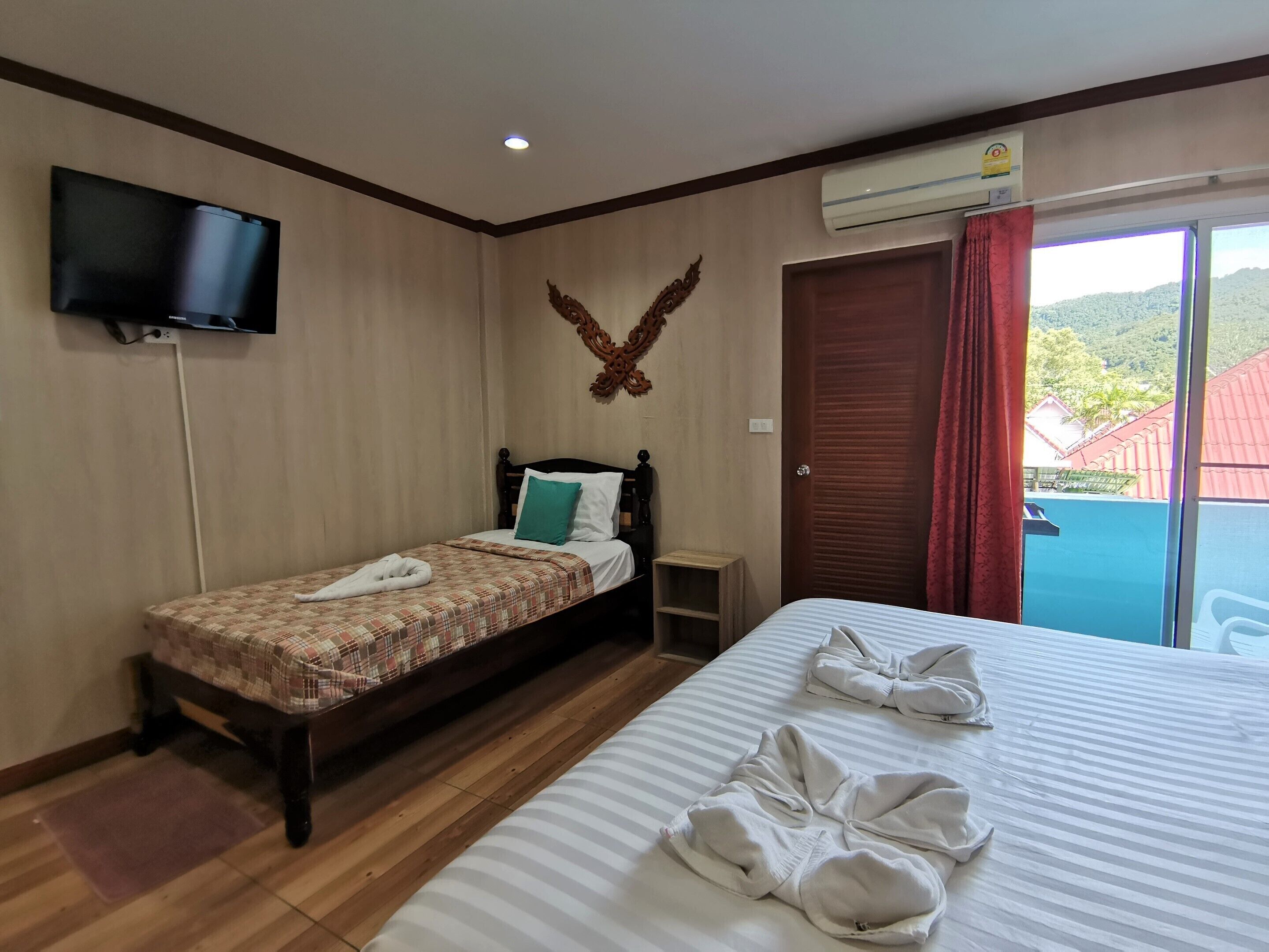 A hotel room with a bed, a TV mounted on the wall, an air conditioning unit, and a view of the outdoors through a door.