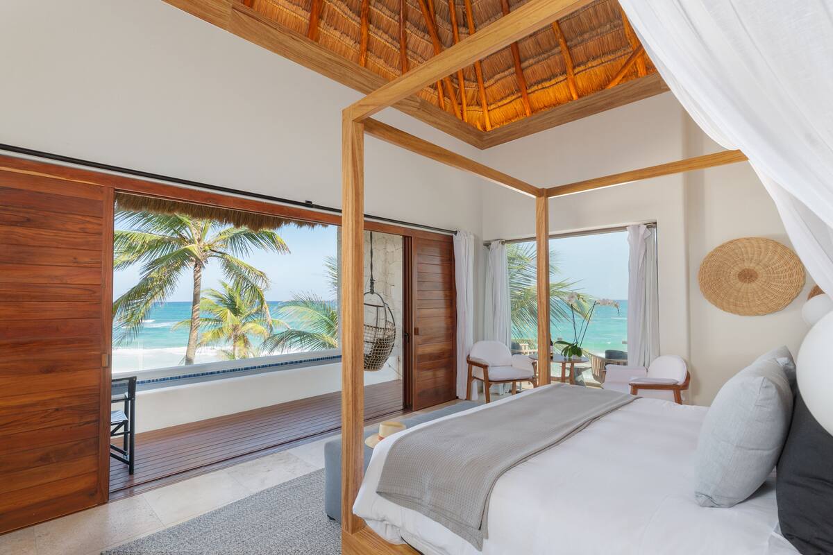 Un dormitorio con una cama grande, vista al océano y un balcón con suelo de madera y una silla colgante.