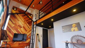 A modern interior with a wooden herringbone floor, a television, a ladder, and a poster on the wall. - Hinoki Mansion (Tainan)