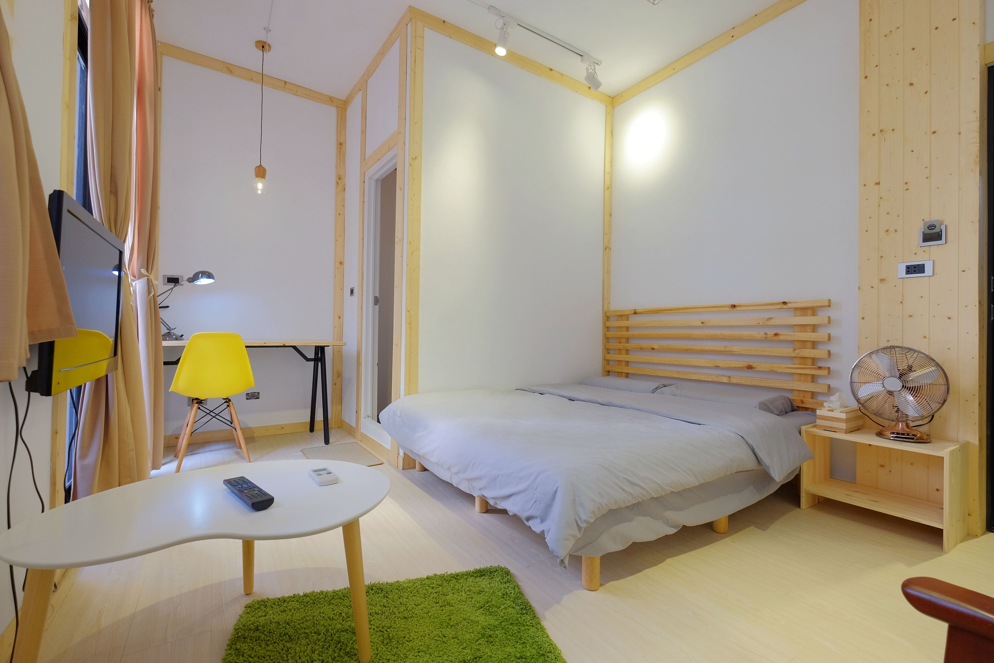 Una camera da letto con un letto, una scrivania, una sedia, una TV e un ventilatore.