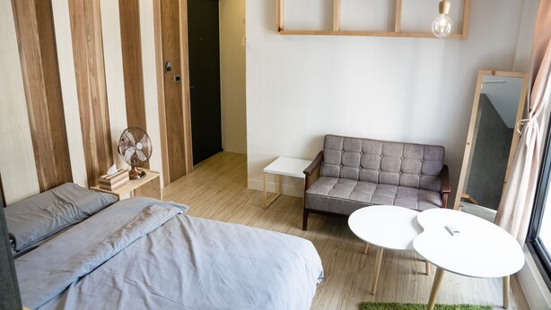 A modern hotel room with a bed, a sofa, two small tables, a fan, and a mirror. - Hinoki Mansion (Tainan)