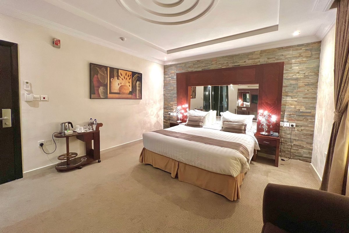 A modern bedroom with a large bed, a desk with a chair, and a stone accent wall.