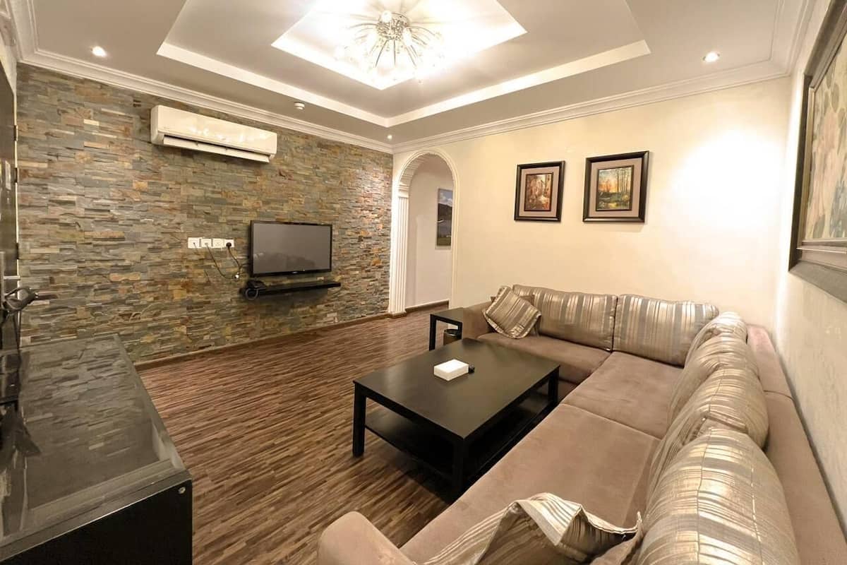 A modern living room with a stone wall, a flat-screen TV, a sectional sofa, and a coffee table.