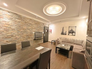 A modern living room with a stone wall, a sofa, a coffee table, and a TV. - loren serviced Apartment Alslamah (Jeddah)