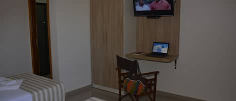 Habitación de hotel con dos camas, un televisor montado en la pared, un ordenador portátil sobre una mesita y una silla con un bolso llamativo.