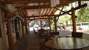 An outdoor patio area with wooden tables and chairs, a brick wall, and a covered seating area. - Hotel Salzburgo (Presidente Franco)