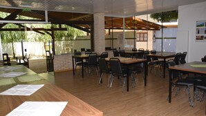 A spacious indoor meeting room with multiple tables and chairs, large windows, and a wooden ceiling. - Hotel Salzburgo (Presidente Franco)