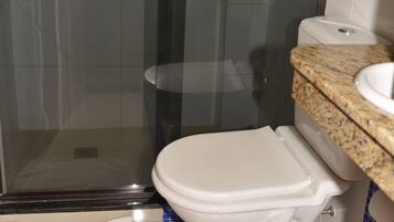 A bathroom with a glass shower enclosure, a white toilet, and a sink with a granite countertop.