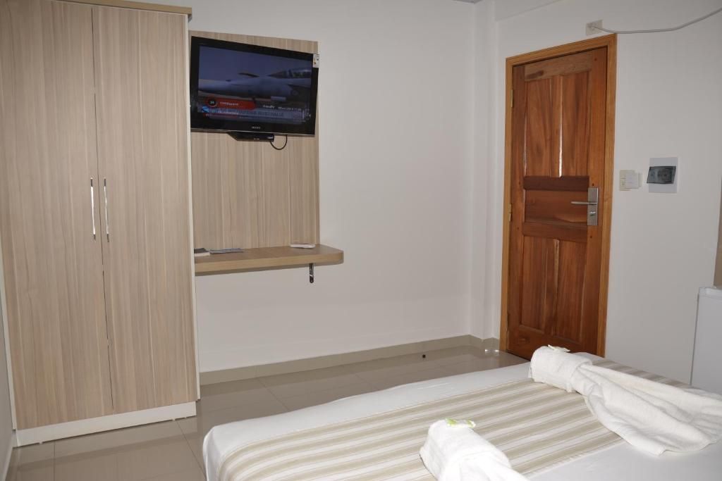 Um quarto com cama, televisão na parede, guarda-roupa e porta de madeira.