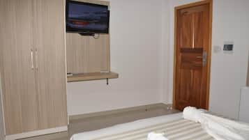 Um quarto com cama, televisão na parede, guarda-roupa e porta de madeira.