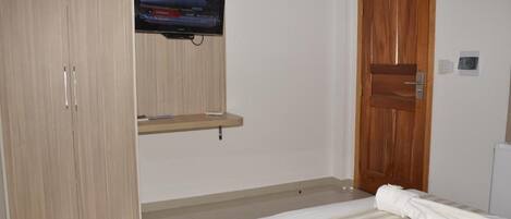 A bedroom with a bed, a television mounted on the wall, a wardrobe, and a wooden door.