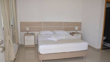 Una cama bien hecha con ropa blanca, cabecera de madera y dos mesitas de noche con lámparas.