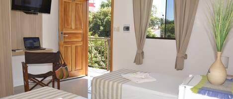 A hotel room with two beds, a desk with a laptop, a TV mounted on the wall, and a balcony with curtains.