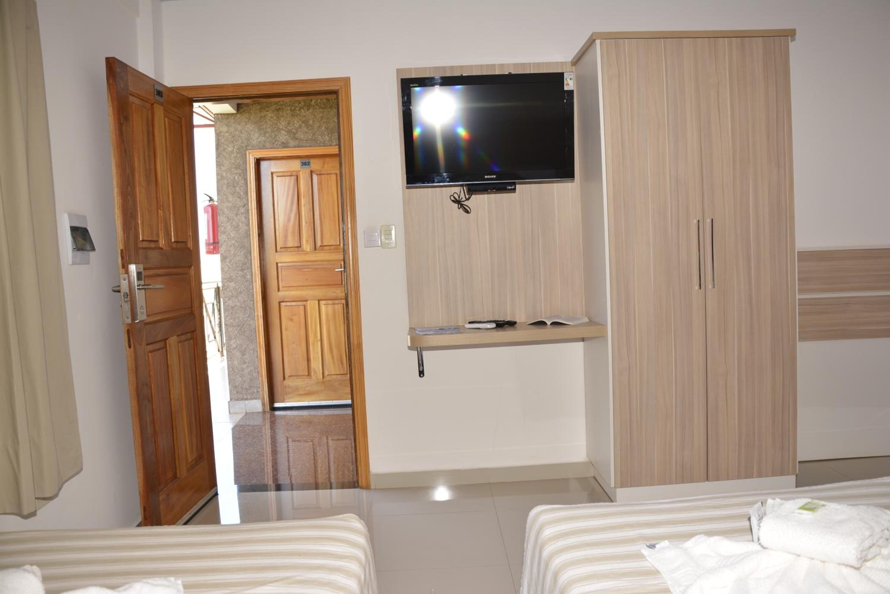 Une chambre d’hôtel avec deux lits, un téléviseur fixé au mur, une armoire en bois et une petite étagère.