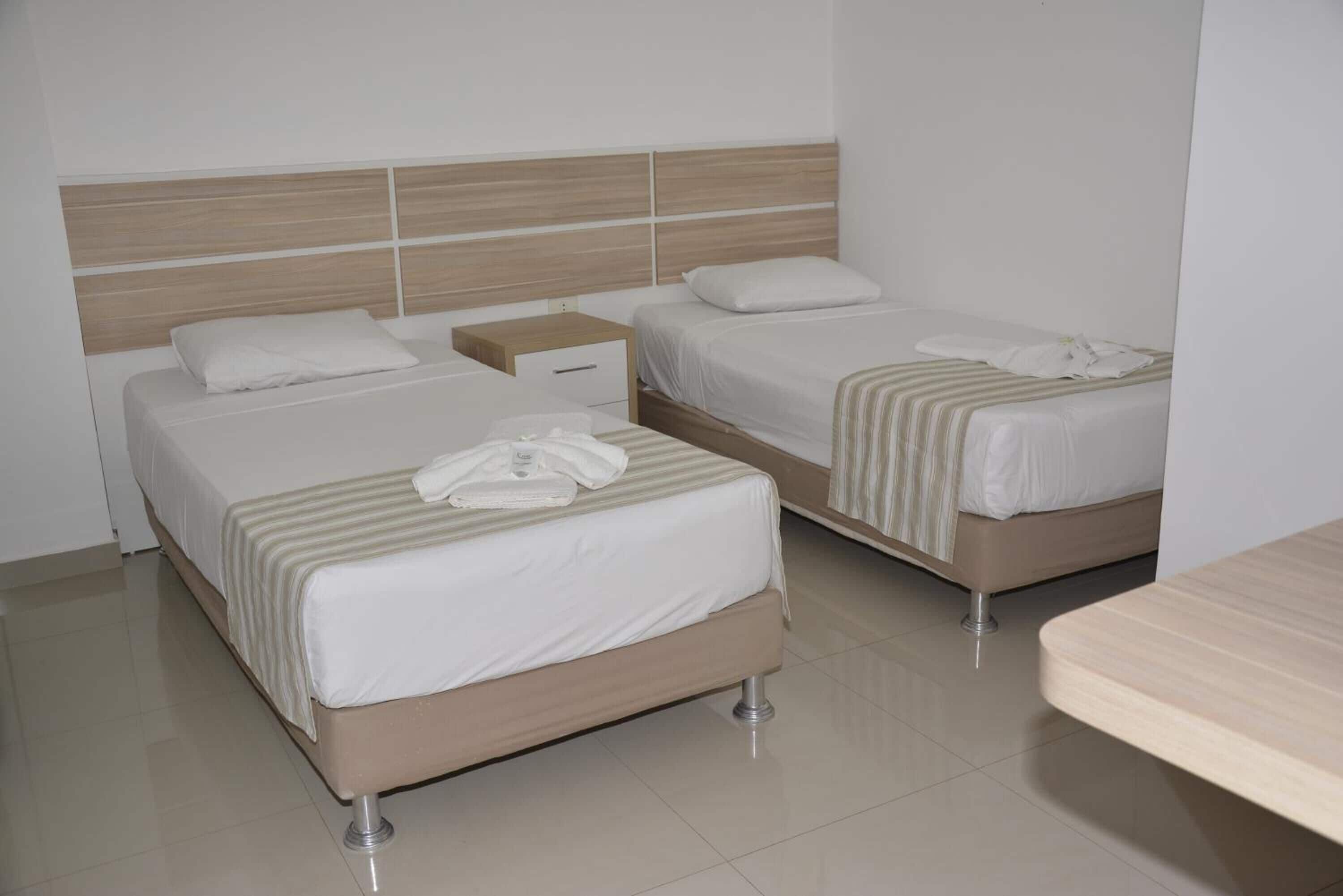 Una habitación de hotel con dos camas, una mesita de noche y un cabecero de madera.