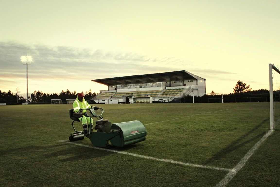 Een sportveld met iemand die een grasmaaier bedient.