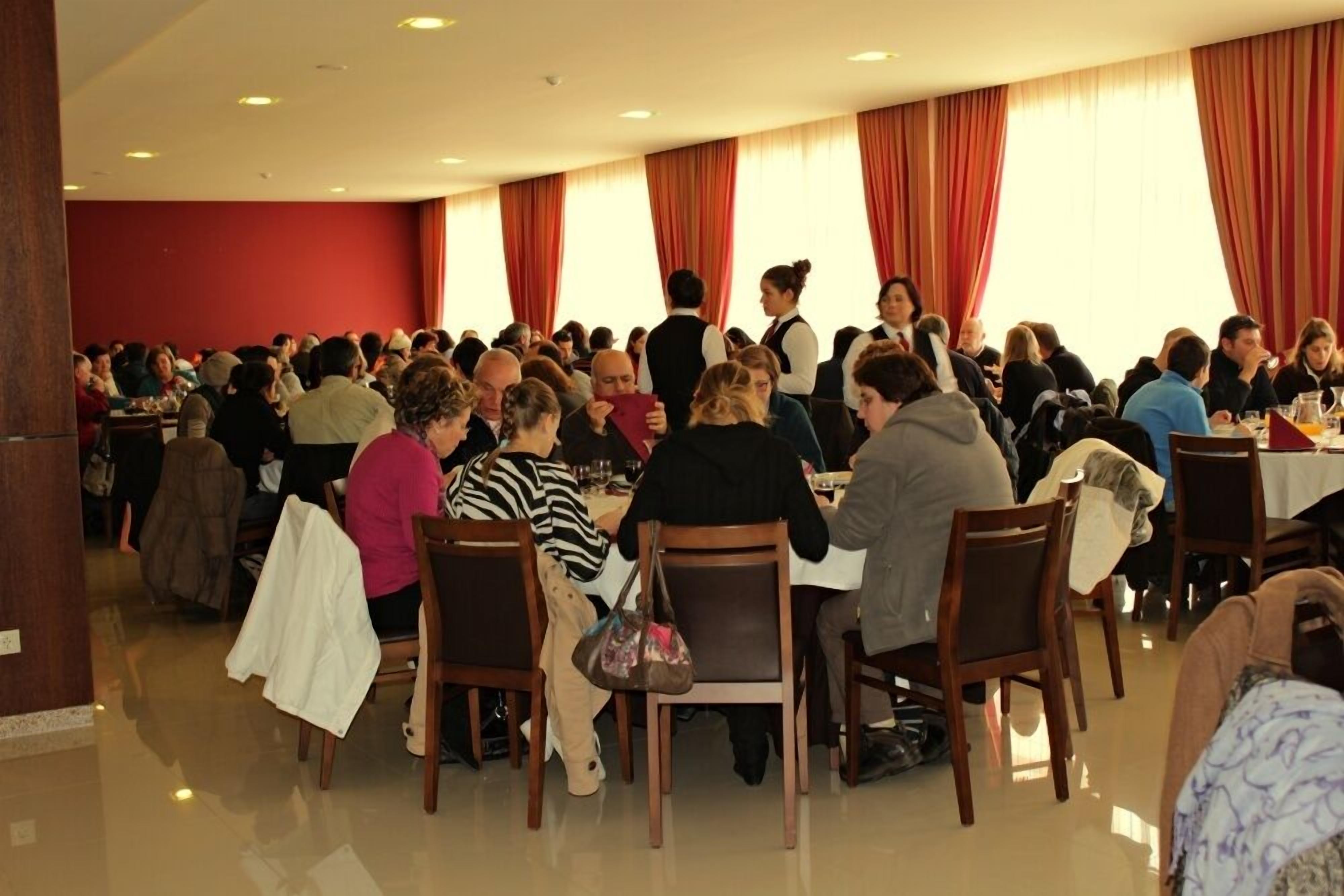 A large indoor dining area with multiple tables and chairs, red curtains, and a polished floor.