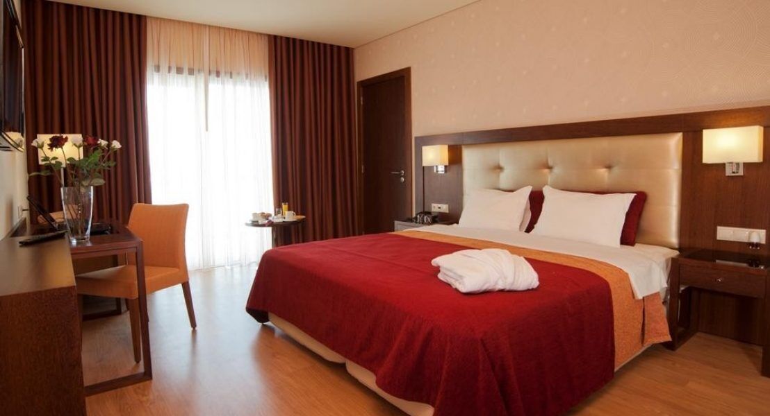 Een hotelkamer met een groot bed, een bureau met stoel, een nachtkastje en een vaas met bloemen.