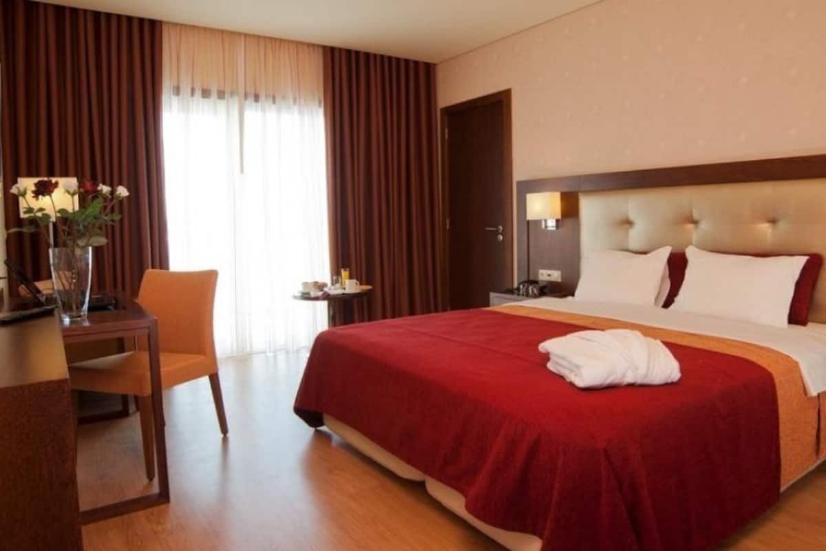 Habitación de hotel con una cama grande, un escritorio con silla, una mesita de noche y un florero con flores.