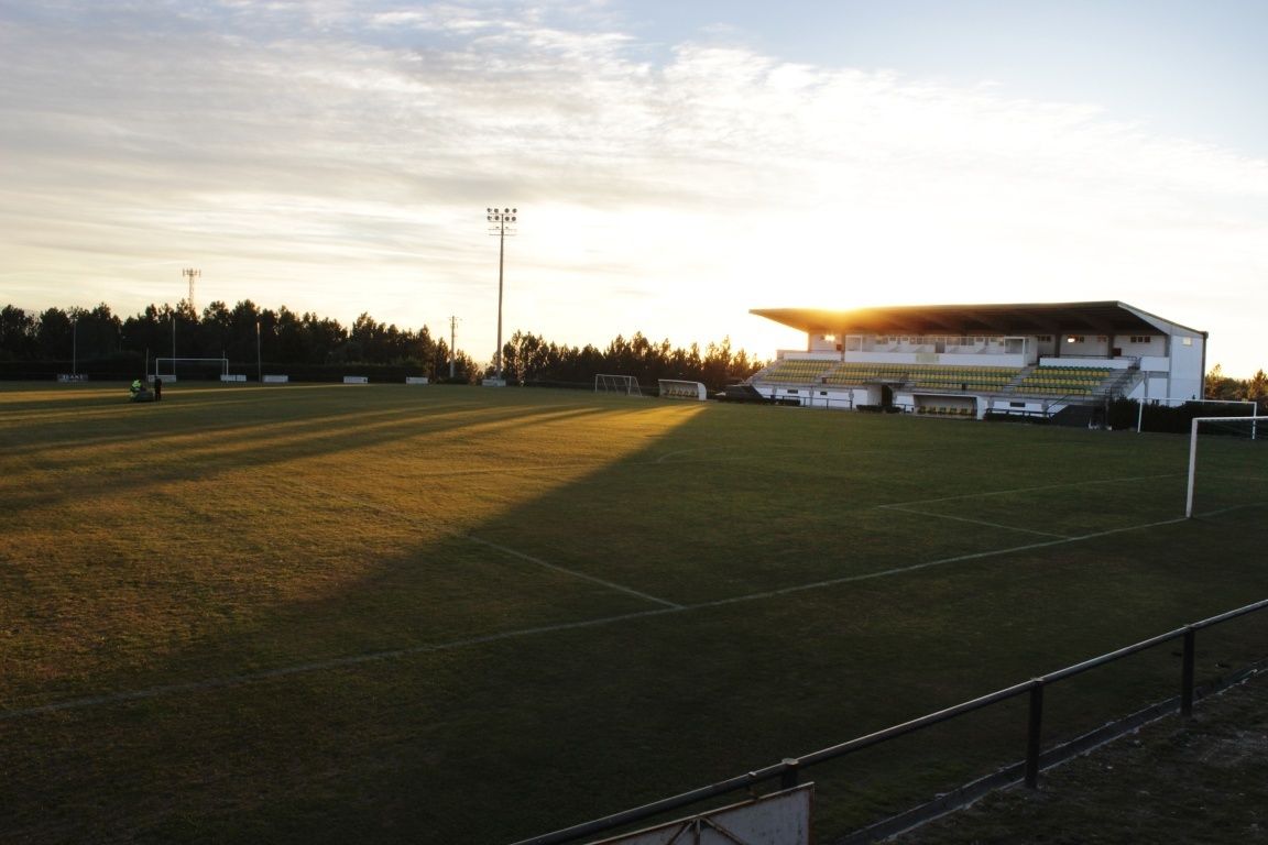 A sports field with goalposts, a floodlight pole, and a building with bleachers.