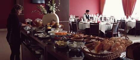 A buffet setup with various food items and a waiter in the background.