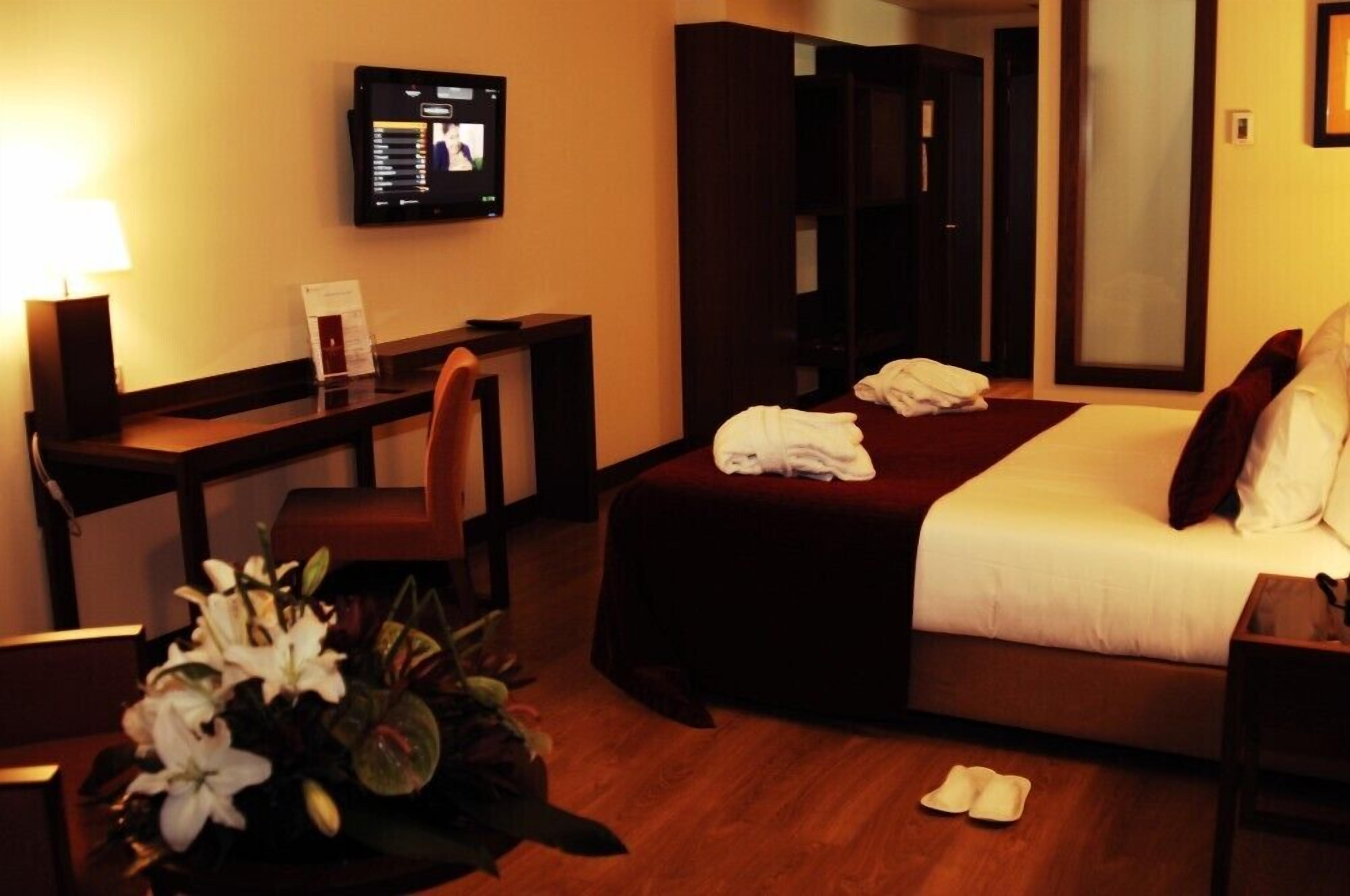 A hotel room with a bed, a desk, a chair, a TV, and a mirror.