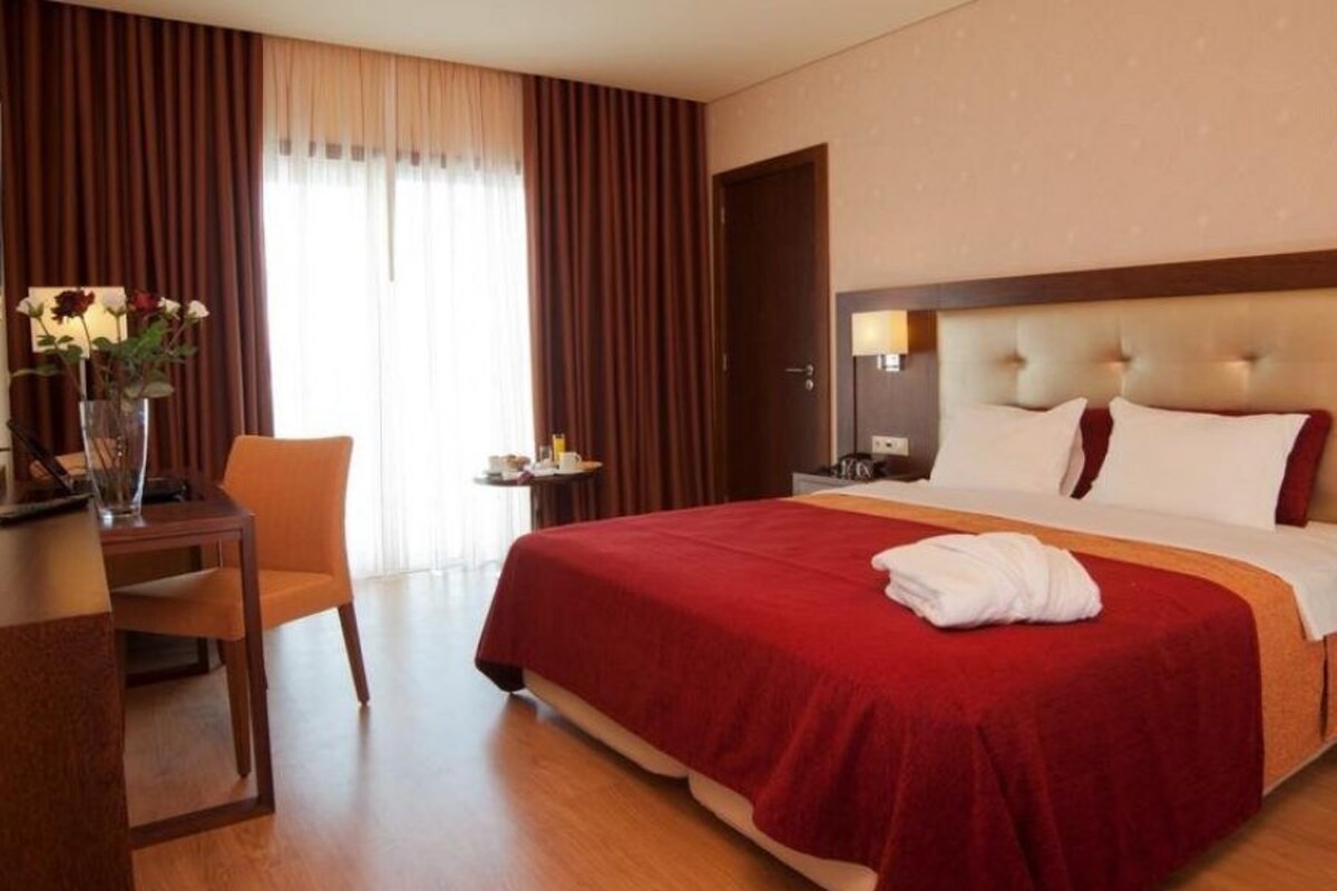 A hotel room with a large bed, a desk with a chair, a nightstand, and a vase with flowers.