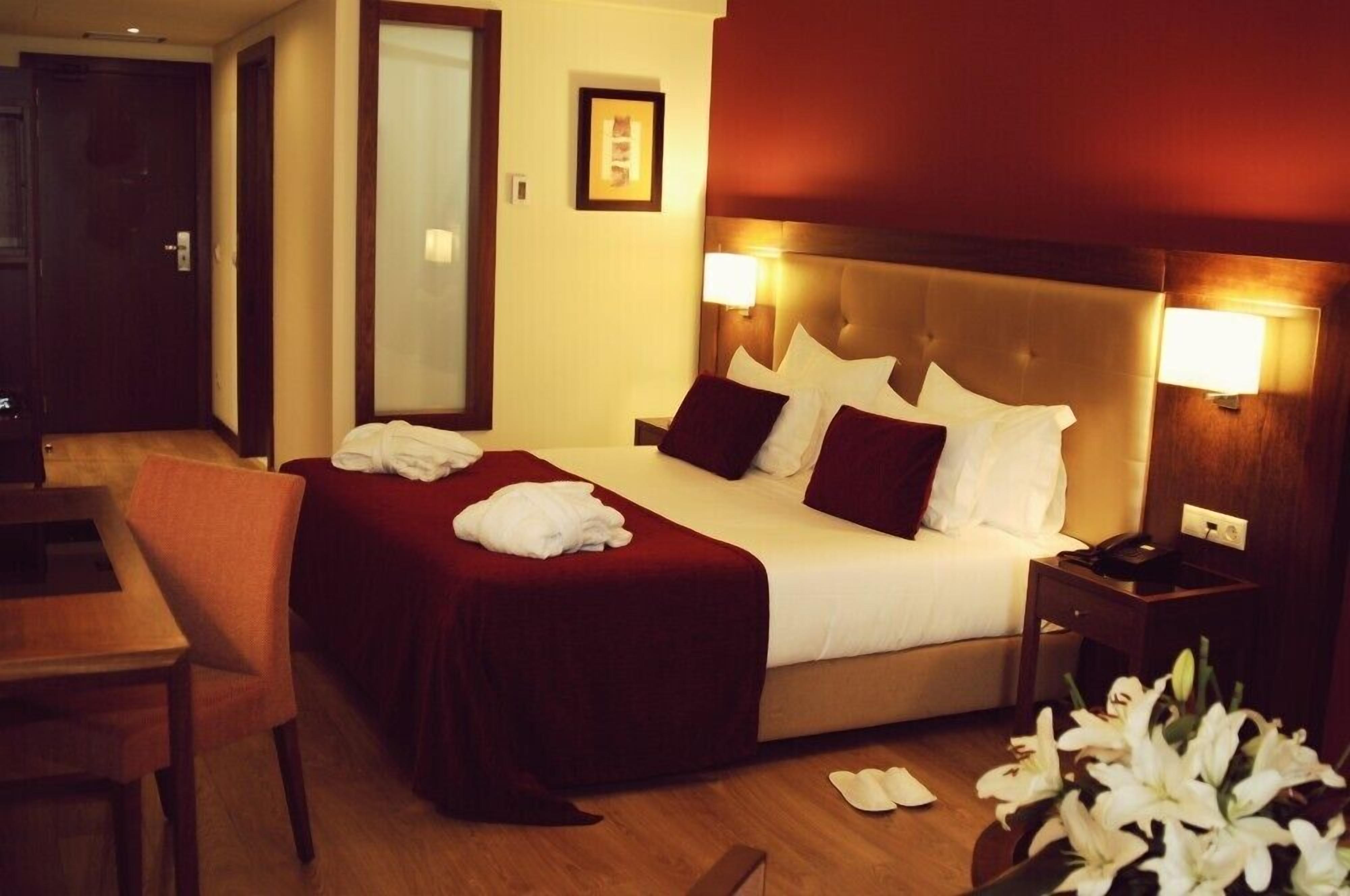 A hotel room with a large bed, a bedside table, a chair, and a desk.