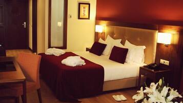 A hotel room with a large bed, a bedside table, a chair, and a desk.