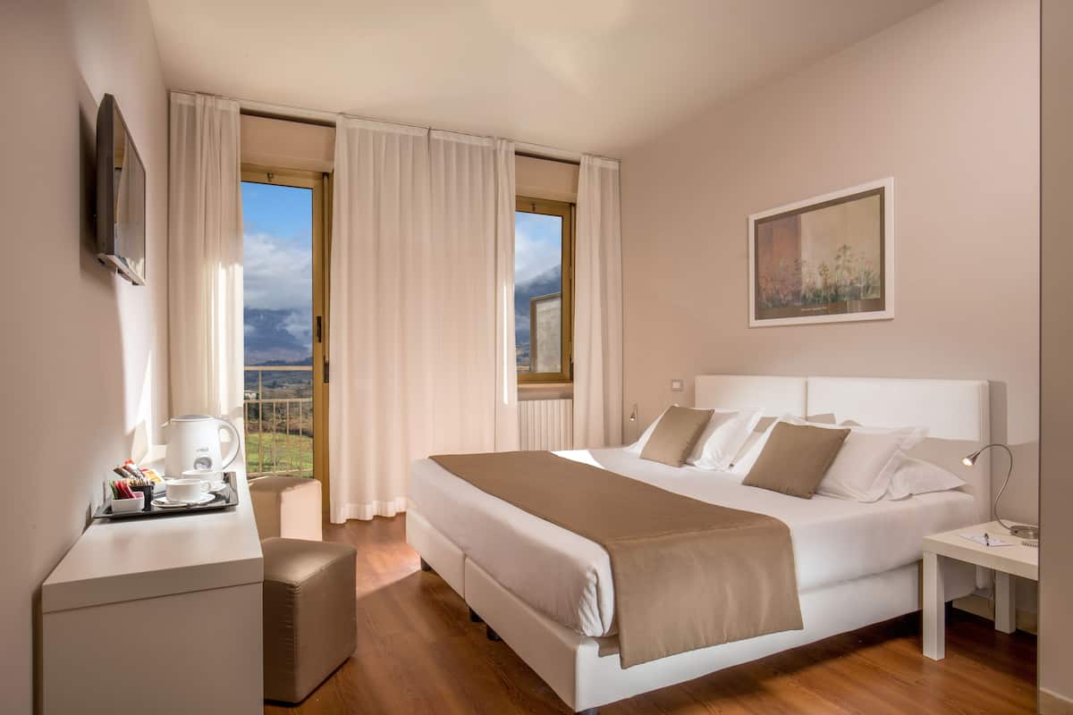 Habitació d'hotel amb un llit gran, una taula de treball amb una cafetera i vista a l'exterior.